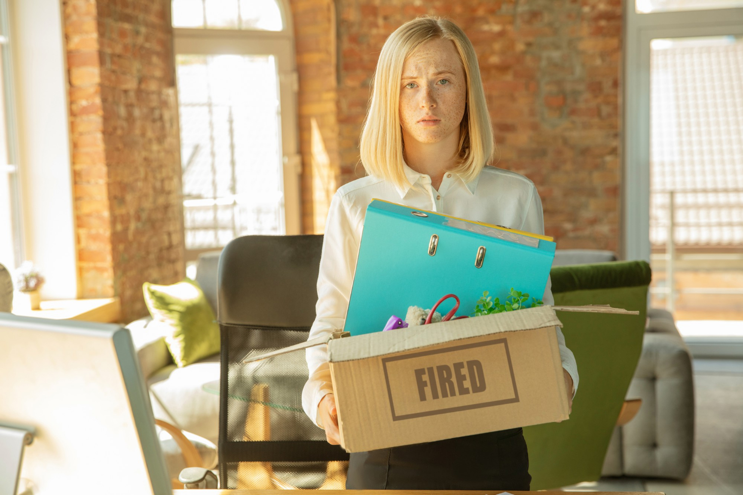 Blonde woman is holding a box with personal stuff - being FIRED.