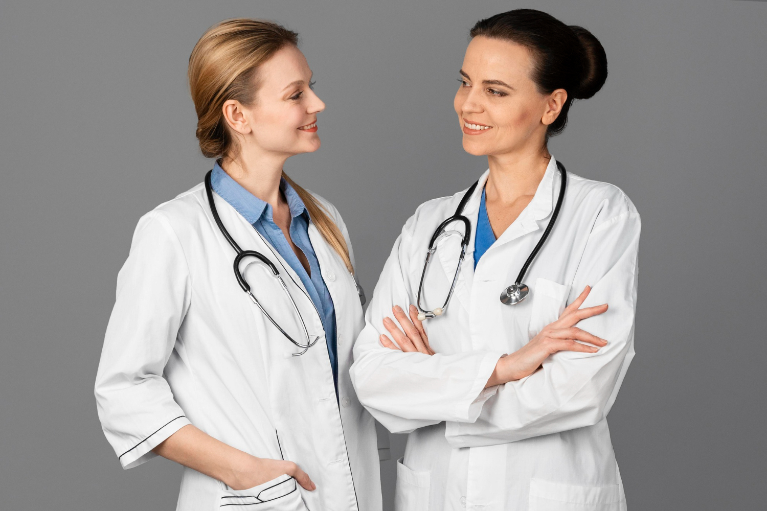 Two female doctors at hospital is talking and smiling on grey background.