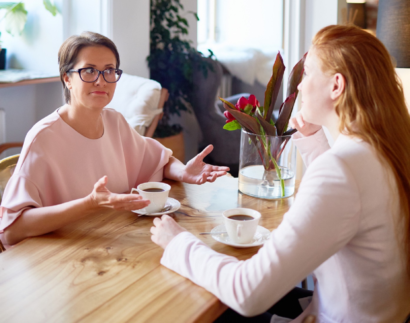 Two young woman are seating at home and drinking coffee.