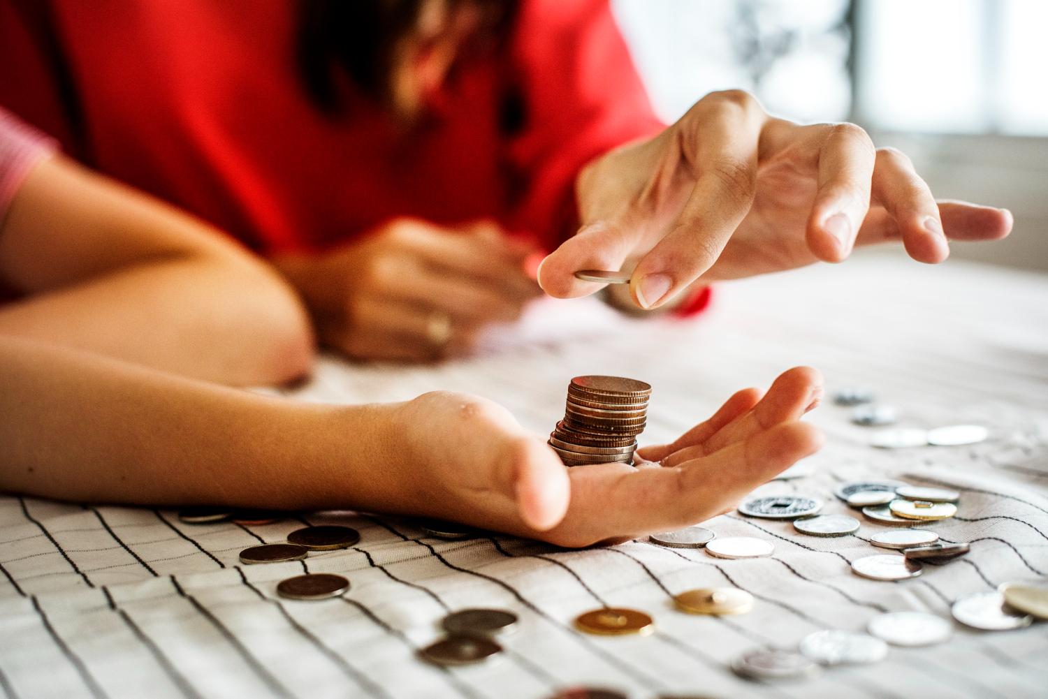 Two woman are counting metal coins on the table.