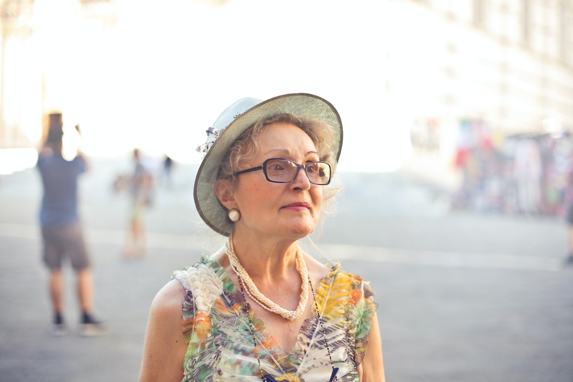 Old lady in flower dress, a hat and pearls standing on a street