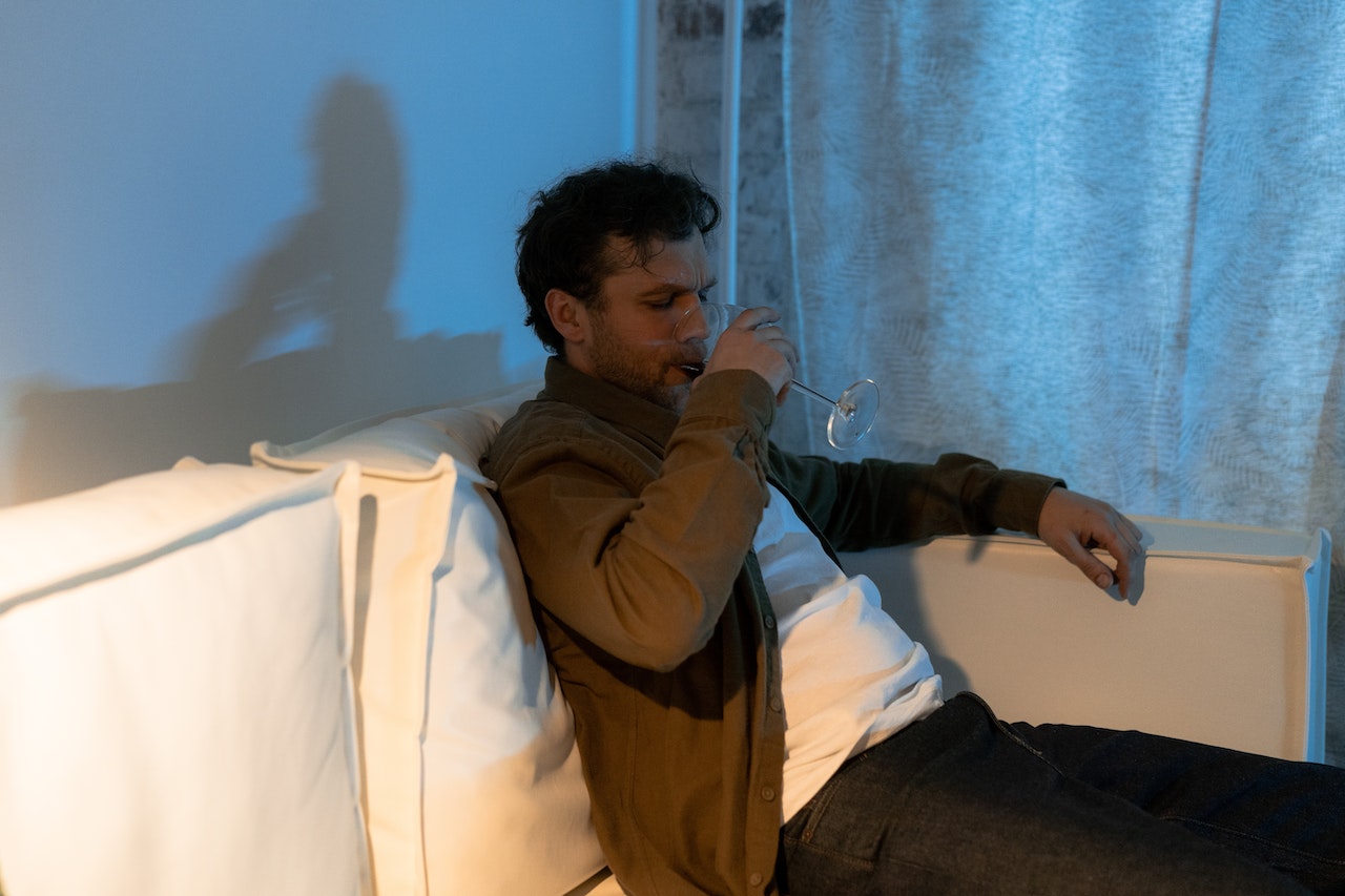 Man is seating on the bed and drinking.