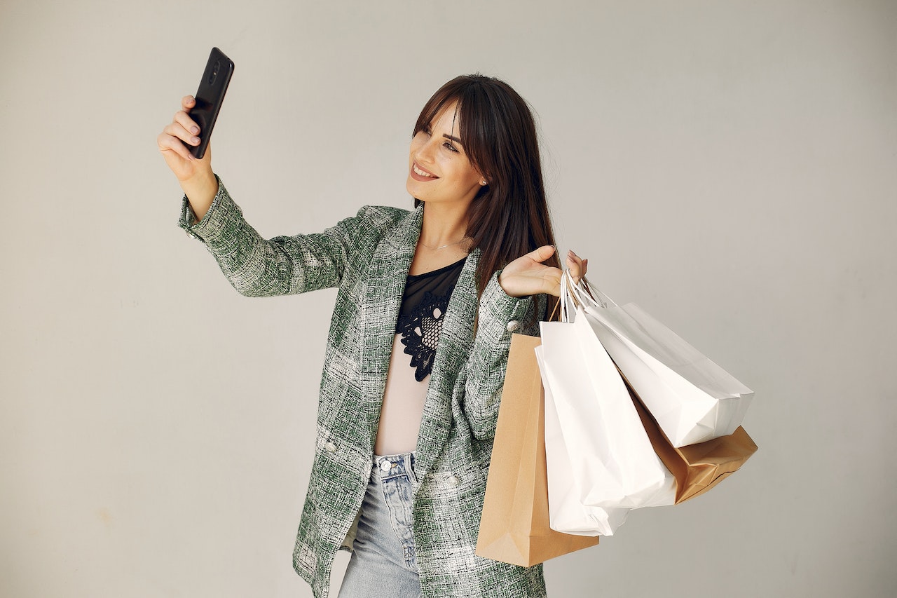 Young woman is holding shopping bags and making a selfie.