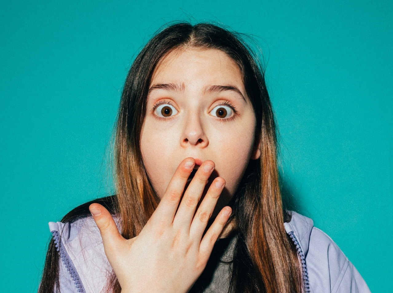 Girl wearing purple jacket is looking at camera with shocked face .