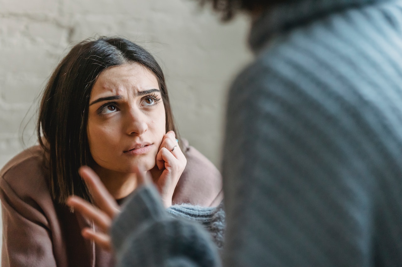 Girl wearing red hoodie is talking with other girl in room.