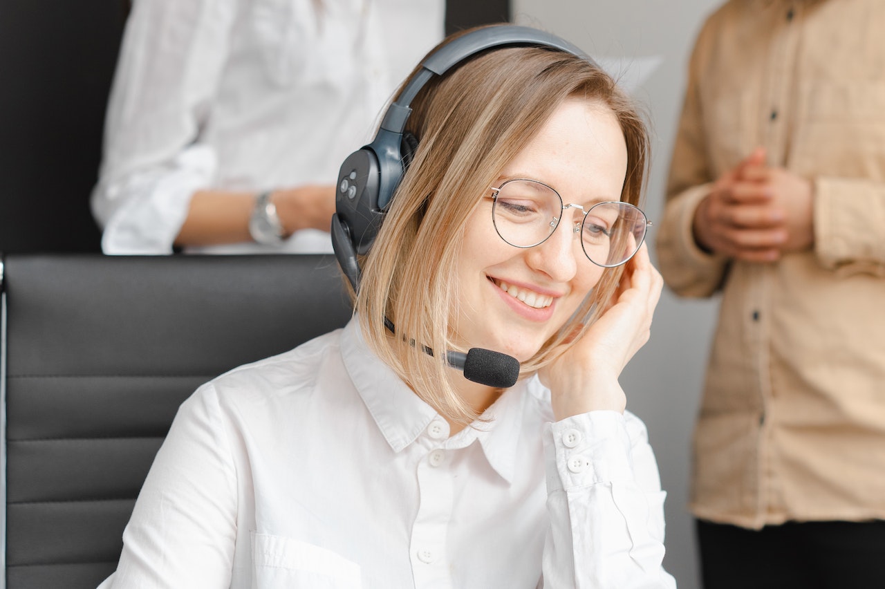Woman wearing black headphone set is smiling and talking with a costumer.