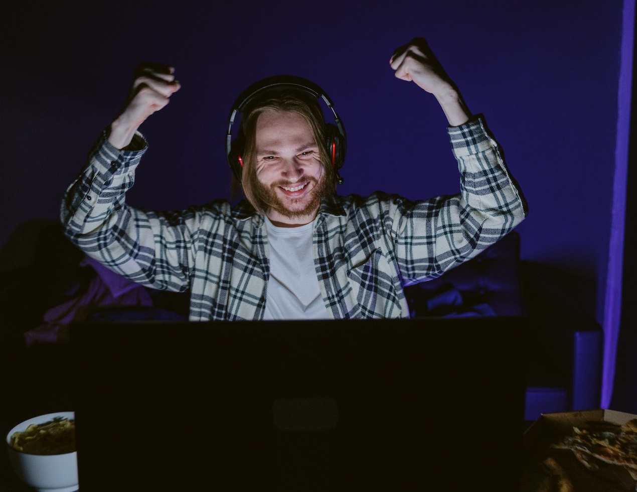 Man is eating pizza and playing computer game in dark room.