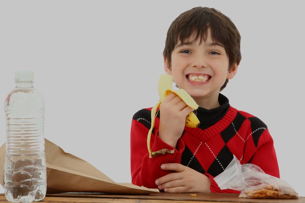 7 year old american boy at a school desk eating a banana