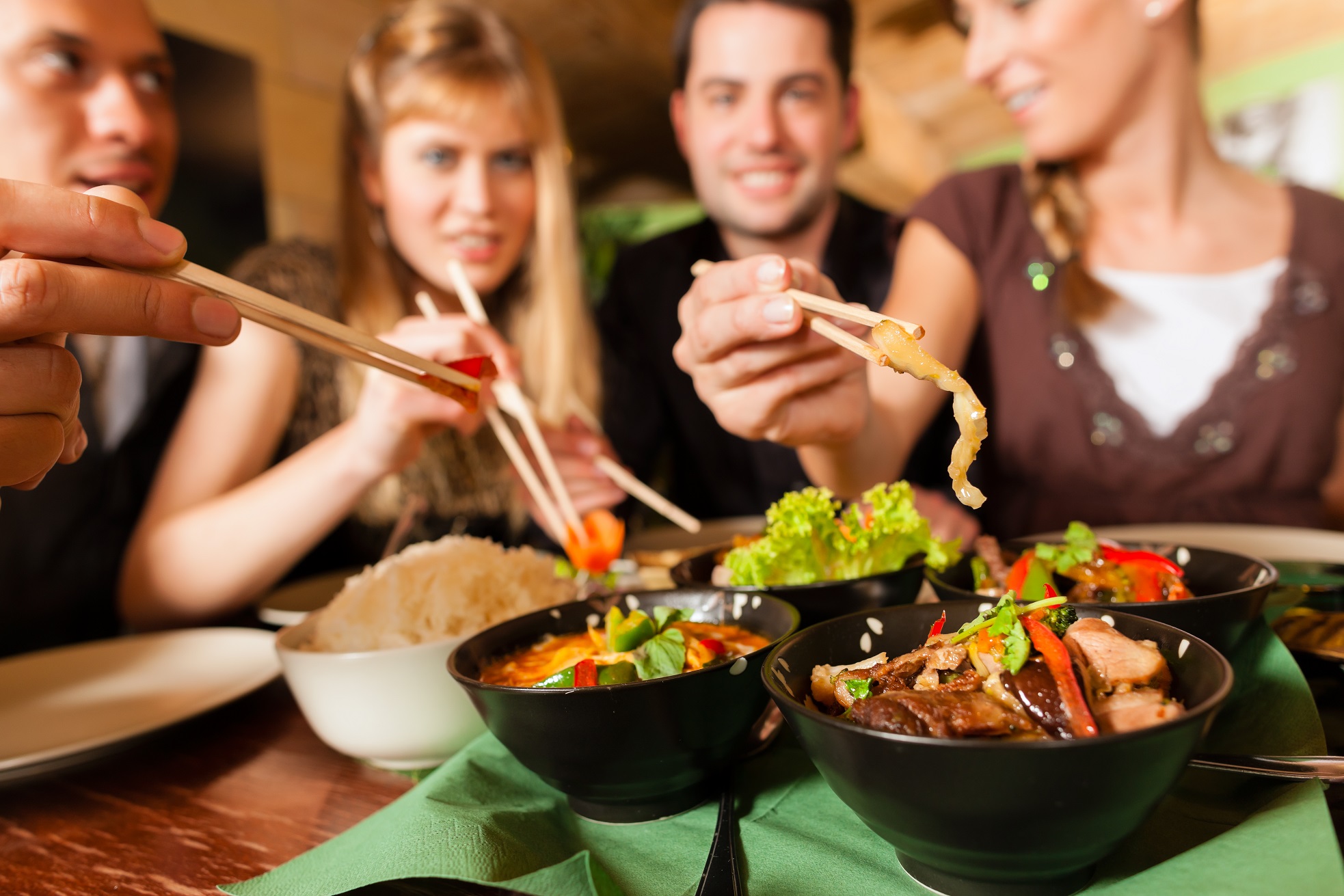 Young people eating in a Thai restaurant with chopsticks.