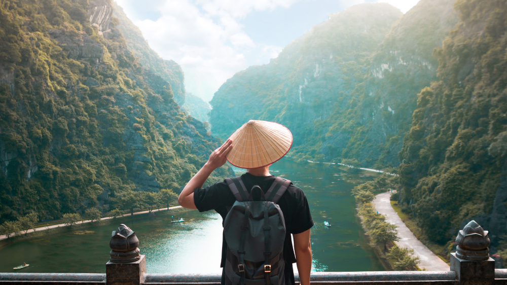 Tourist man is wearing Vietnamese traditional hat and backpack looking at the river
