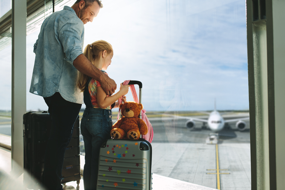 Man with his daughter standing by a large window at airport terminal