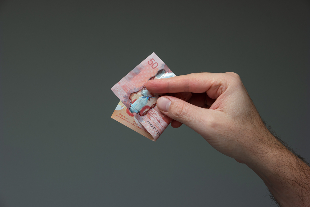 Caucasian male hand holding a folded 50 Canadian dollar bill