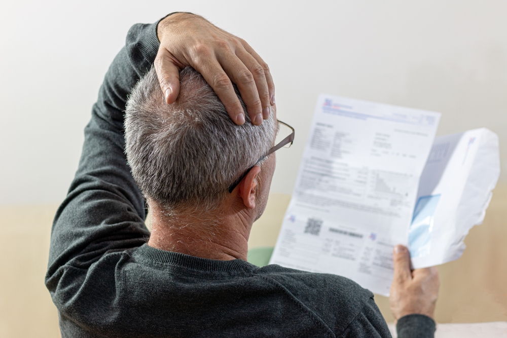 Worried middle-aged man reading unexpected news in paper document  for debt notification
