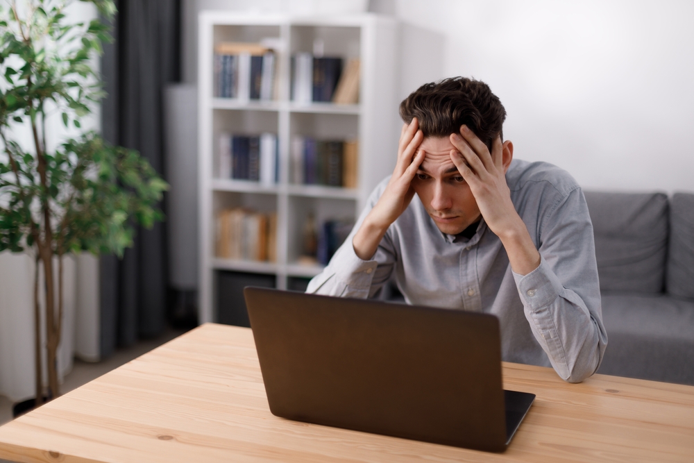 Frustrated Caucasian man in casual clothes getting bad news on modern laptop