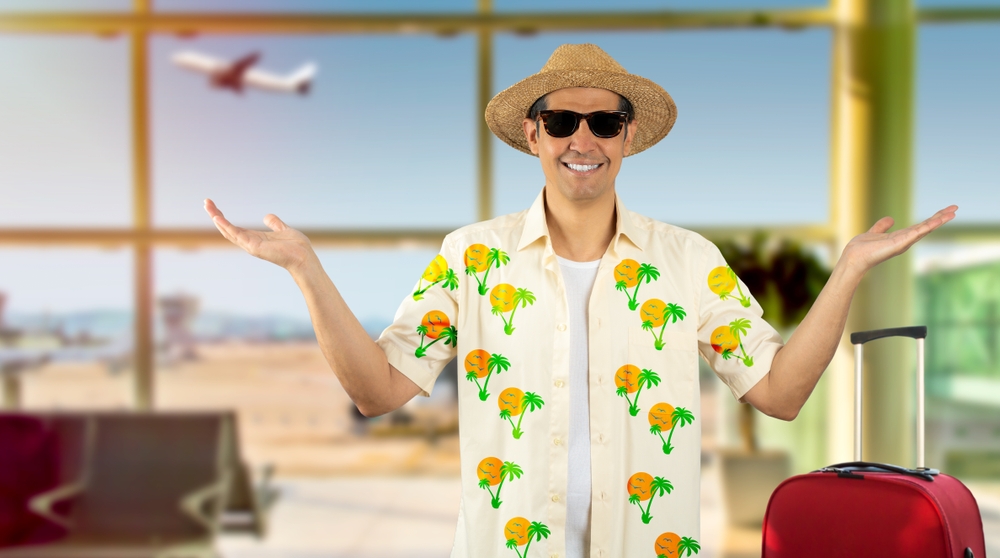 Latin man on vacation wearing floral shirt hat sunglasses at airport confused