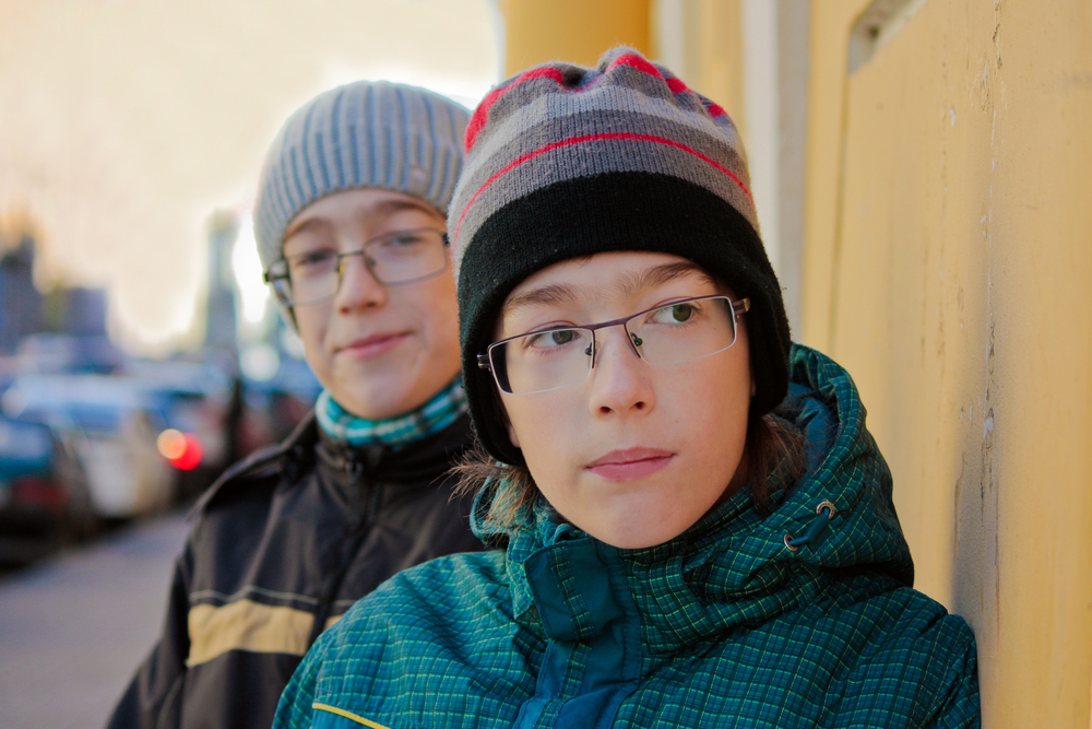 two boys are hiding around the corner of the building