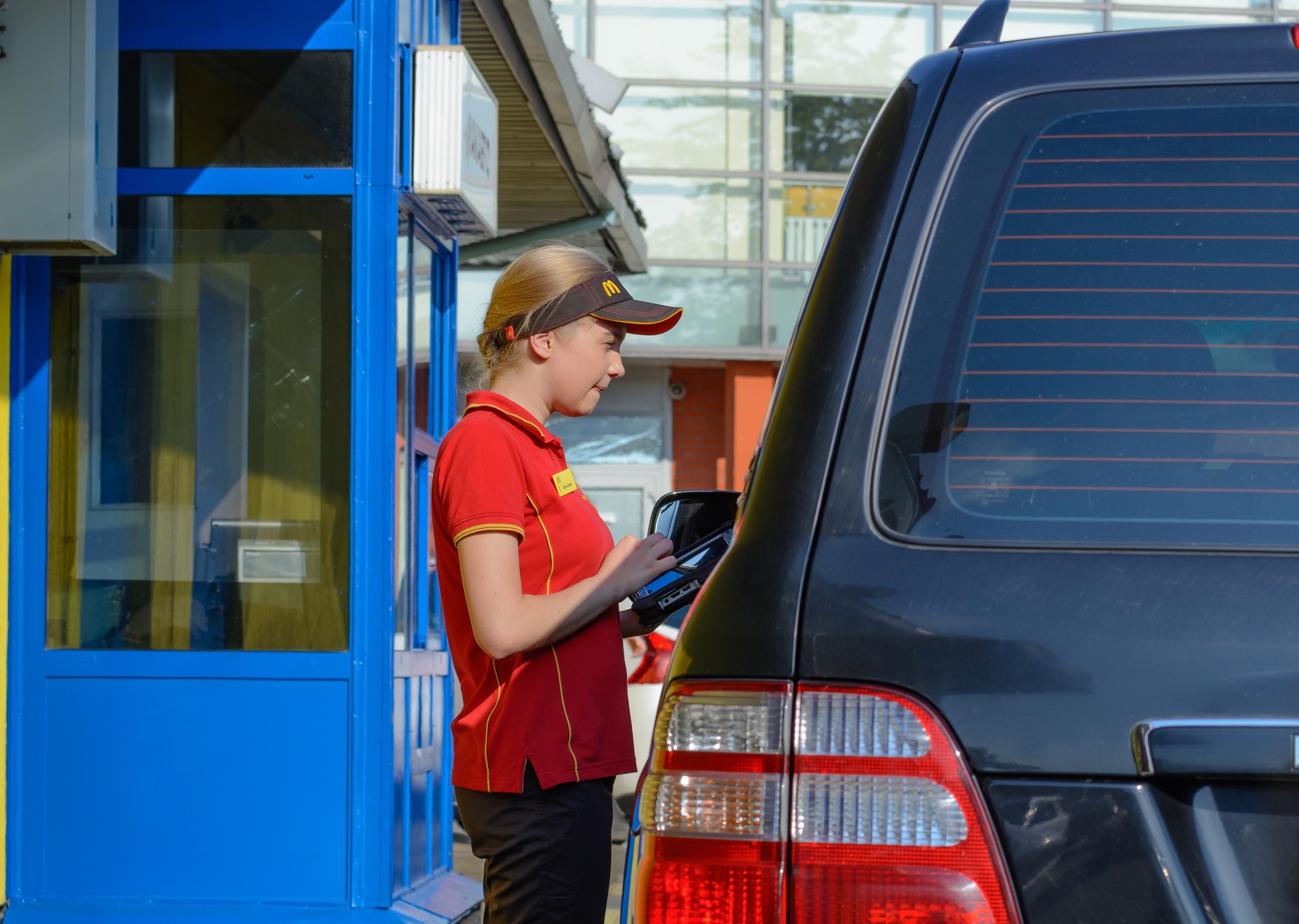 Girl wearing red Mcdonald's uniform is taking an order from customer at drive thru service.