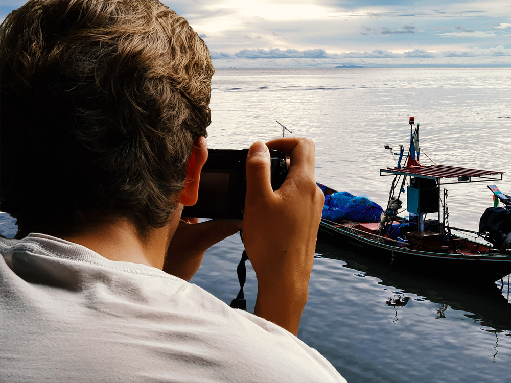 Back view of man taking photo of boat