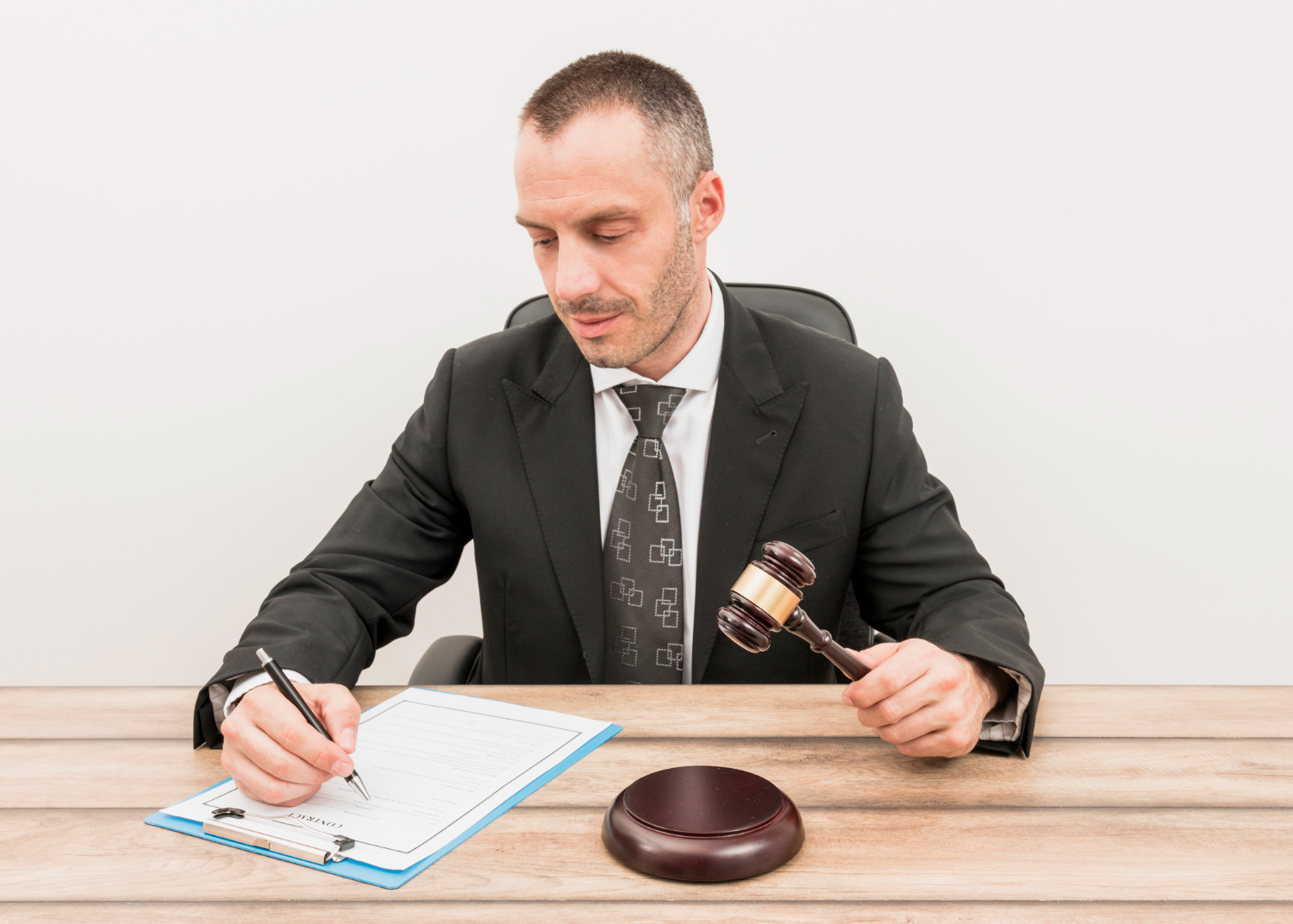 Man is holding a pen ,seating on the bench with a judge hammer in his hand.