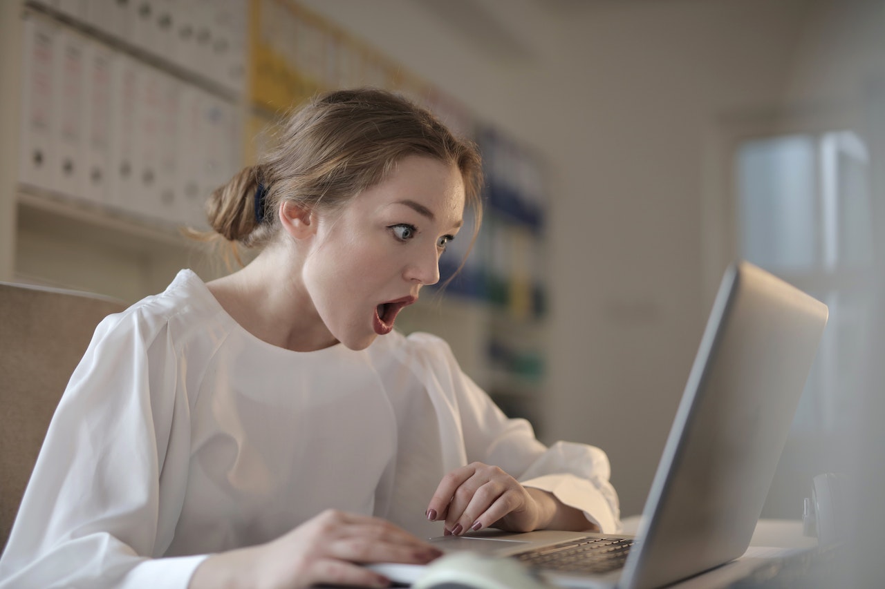 Young woman is looking shocked, looking at her laptop screen.