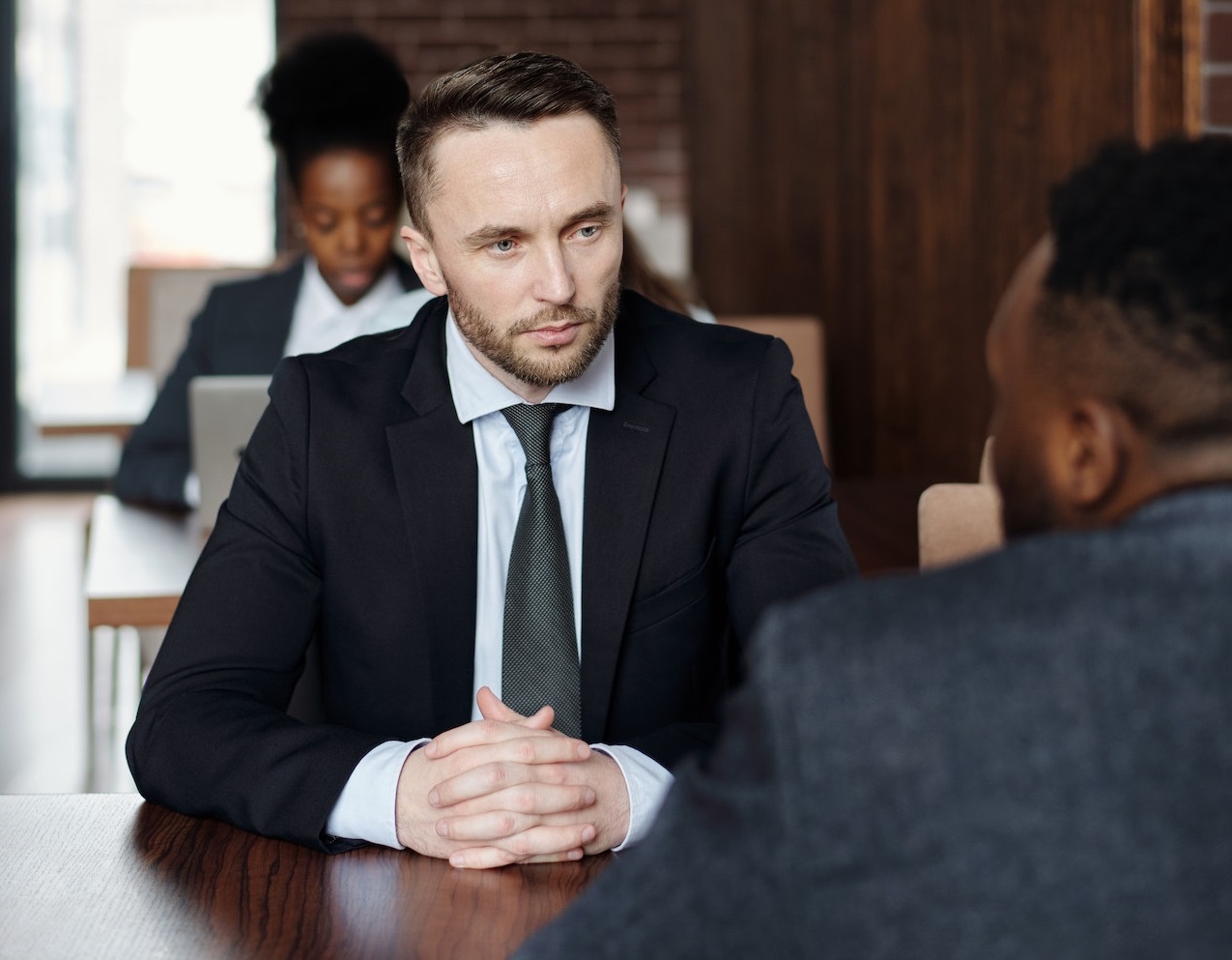 Two man wearing dark suits are talking about work at restaurant.