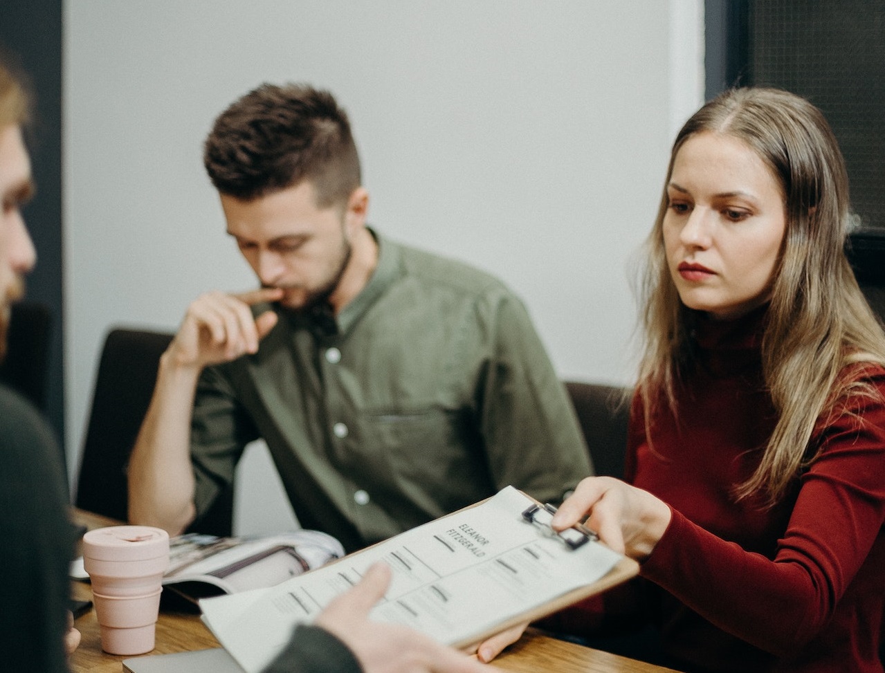 Young man is looking down with sad face seating next to a woman holding documents at office.