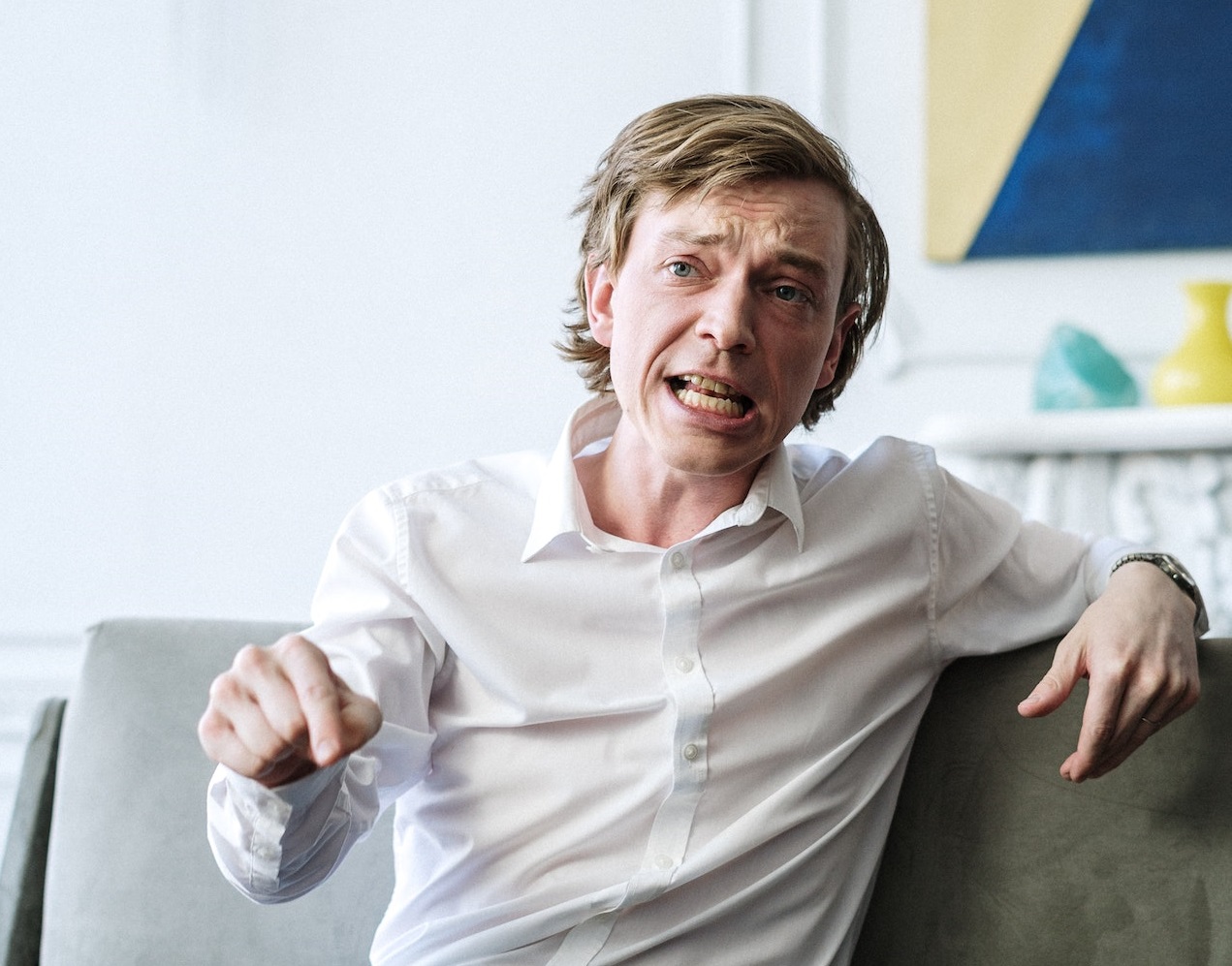 Man seating on the sofa and making a hand gestures with upset face.