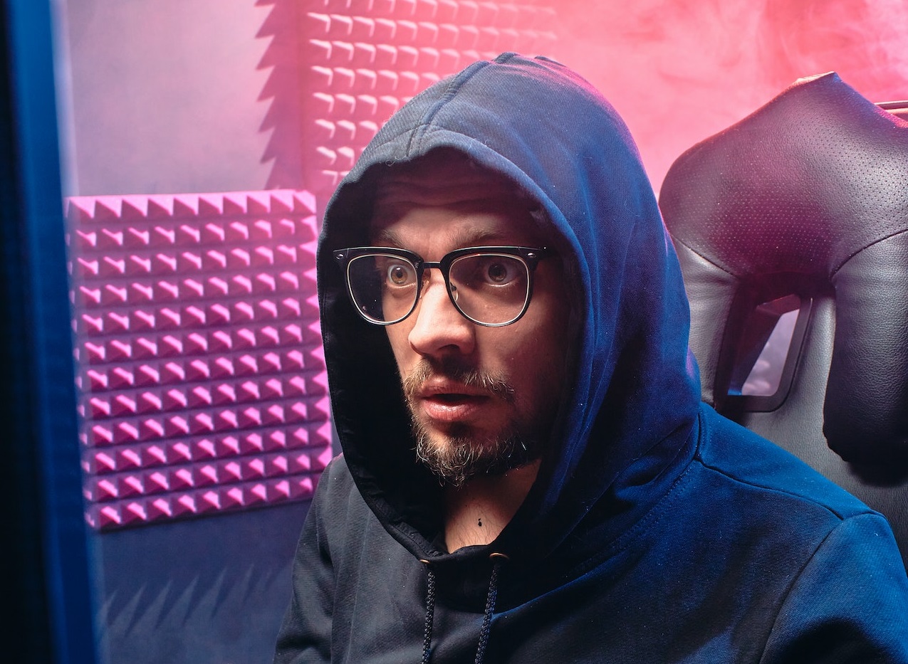Young man wearing black hoodie and glasses is looking at PC screen.