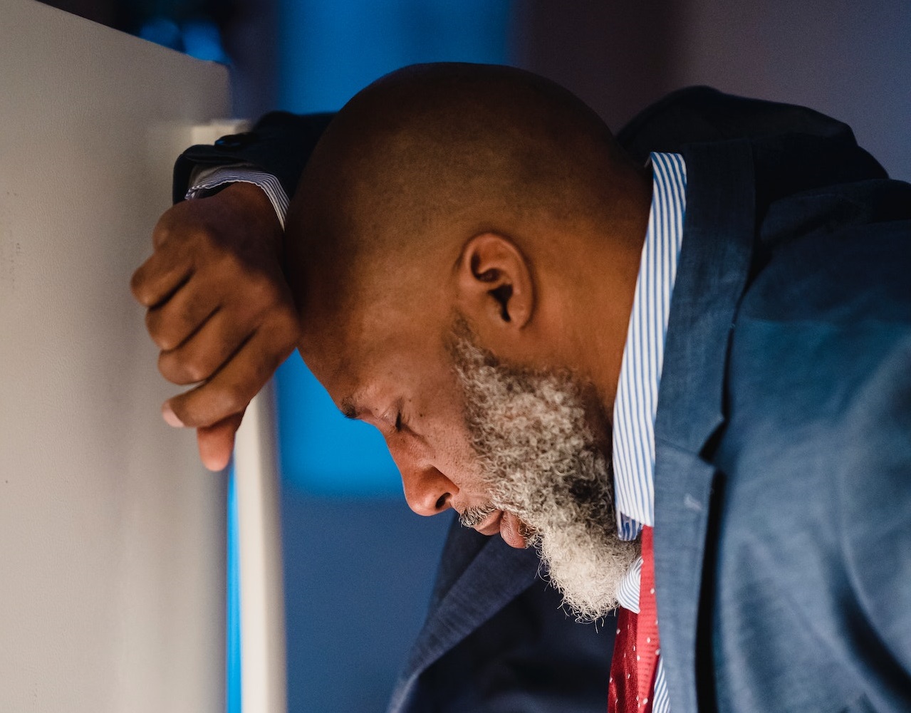 Senior black man is standing next to a wall ,looking sad.