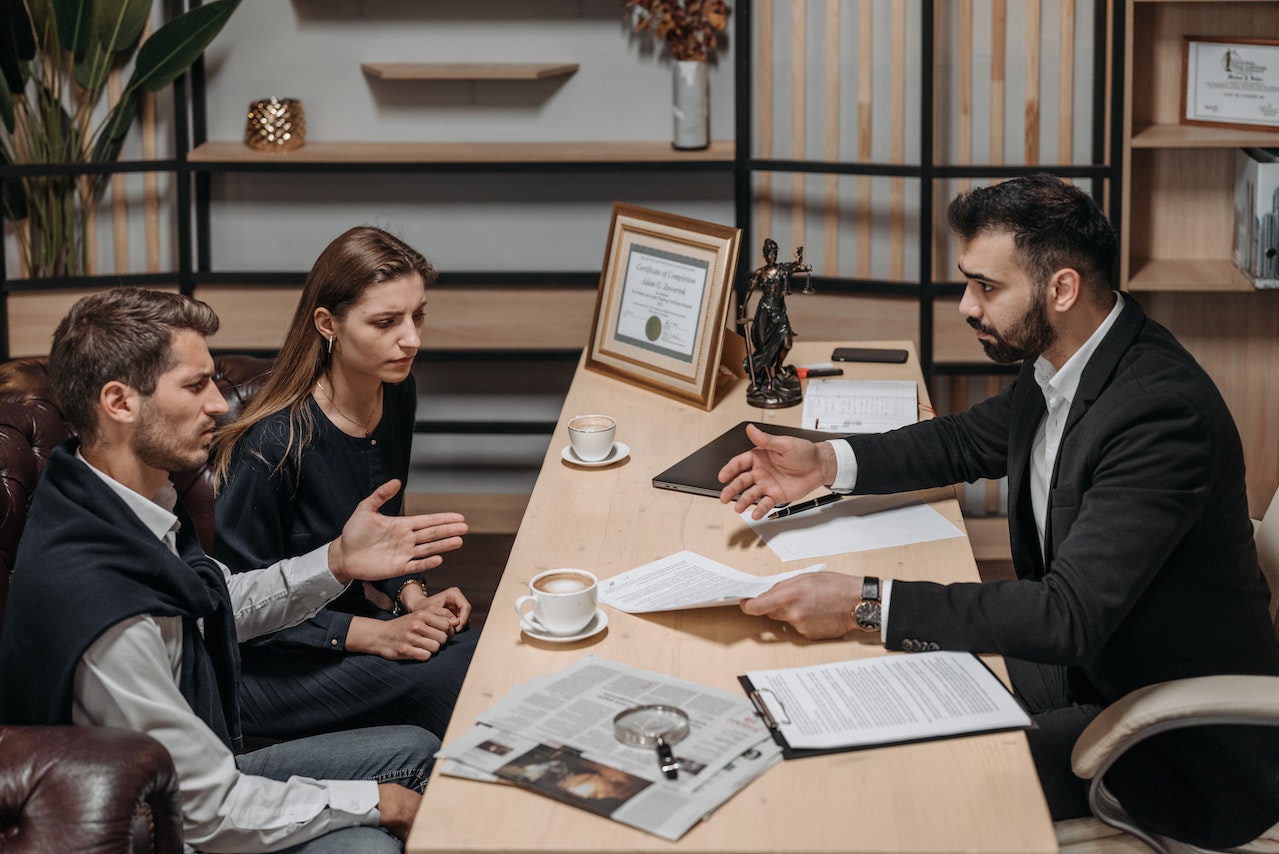 Young couple are seating and talking with lawyer at his office.