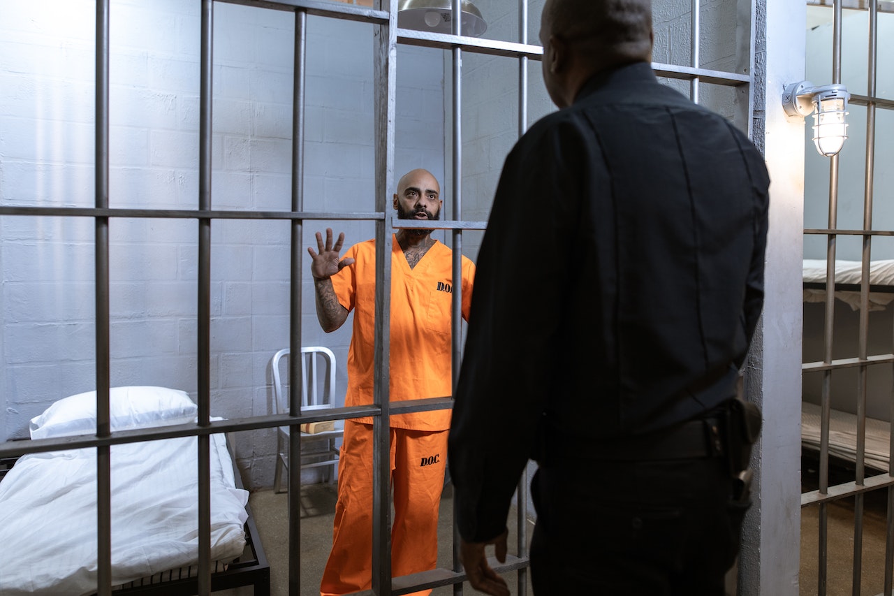 A prisoner in orange suit is talking with a police officer.