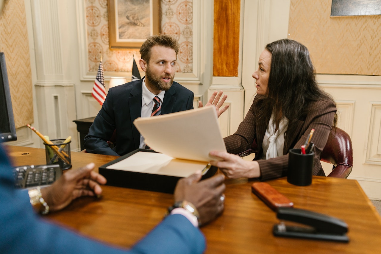 Man and woman are holding a document and arguing between them with man seating in office.