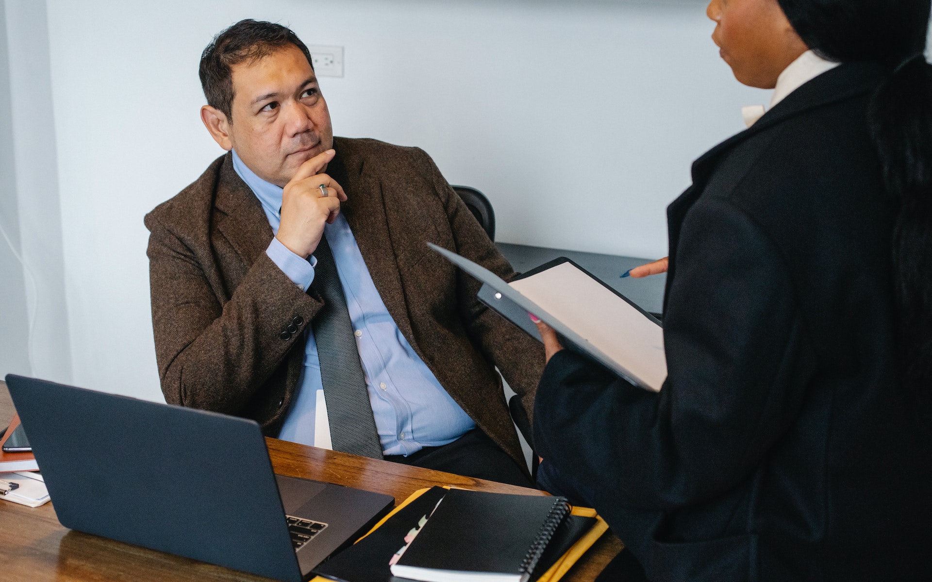Senior man is seating in the office and talking with female holding a documents.