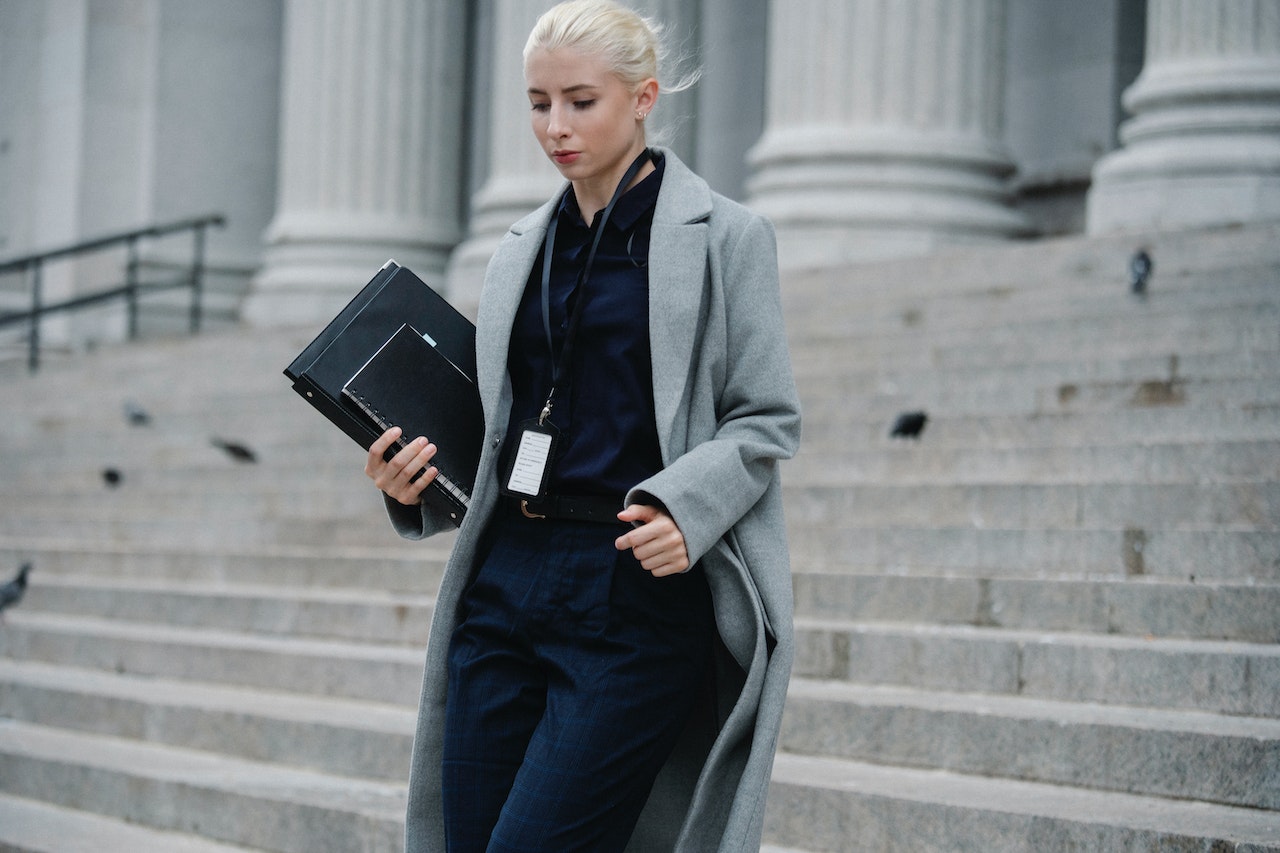 Young blond woman is walking down on stairs from a building ,holding a documents at her hands.