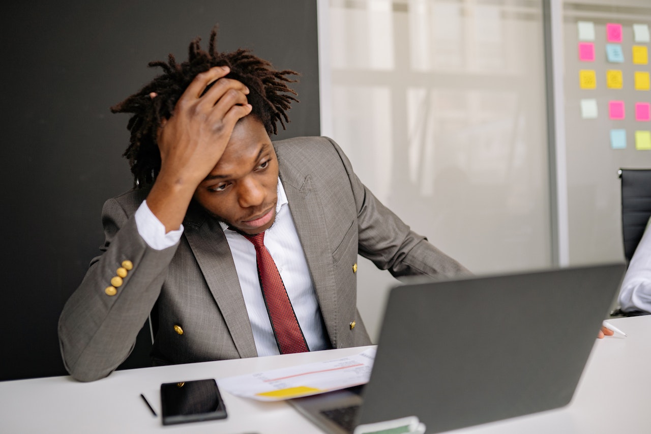 Man is looking at his laptop and holding his head with sad face at office.