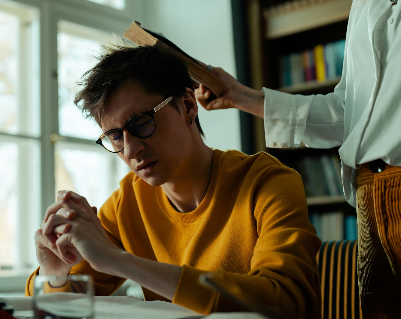 Young male is getting smacked in the head with a book.