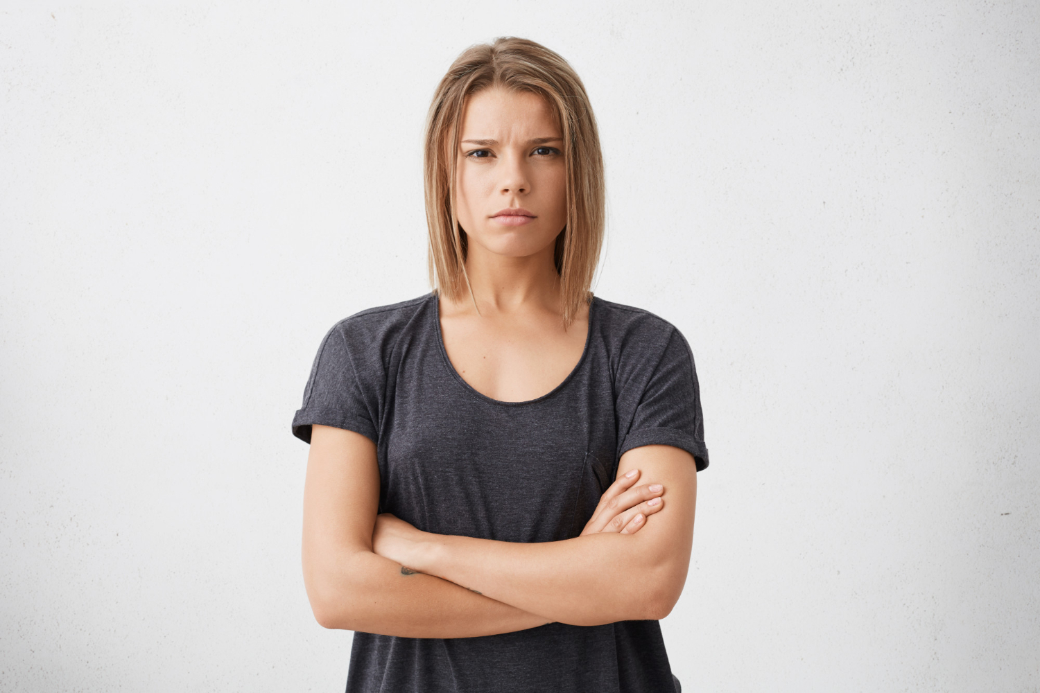 Woman with crossed arms is having a cold look at camera on grey background.