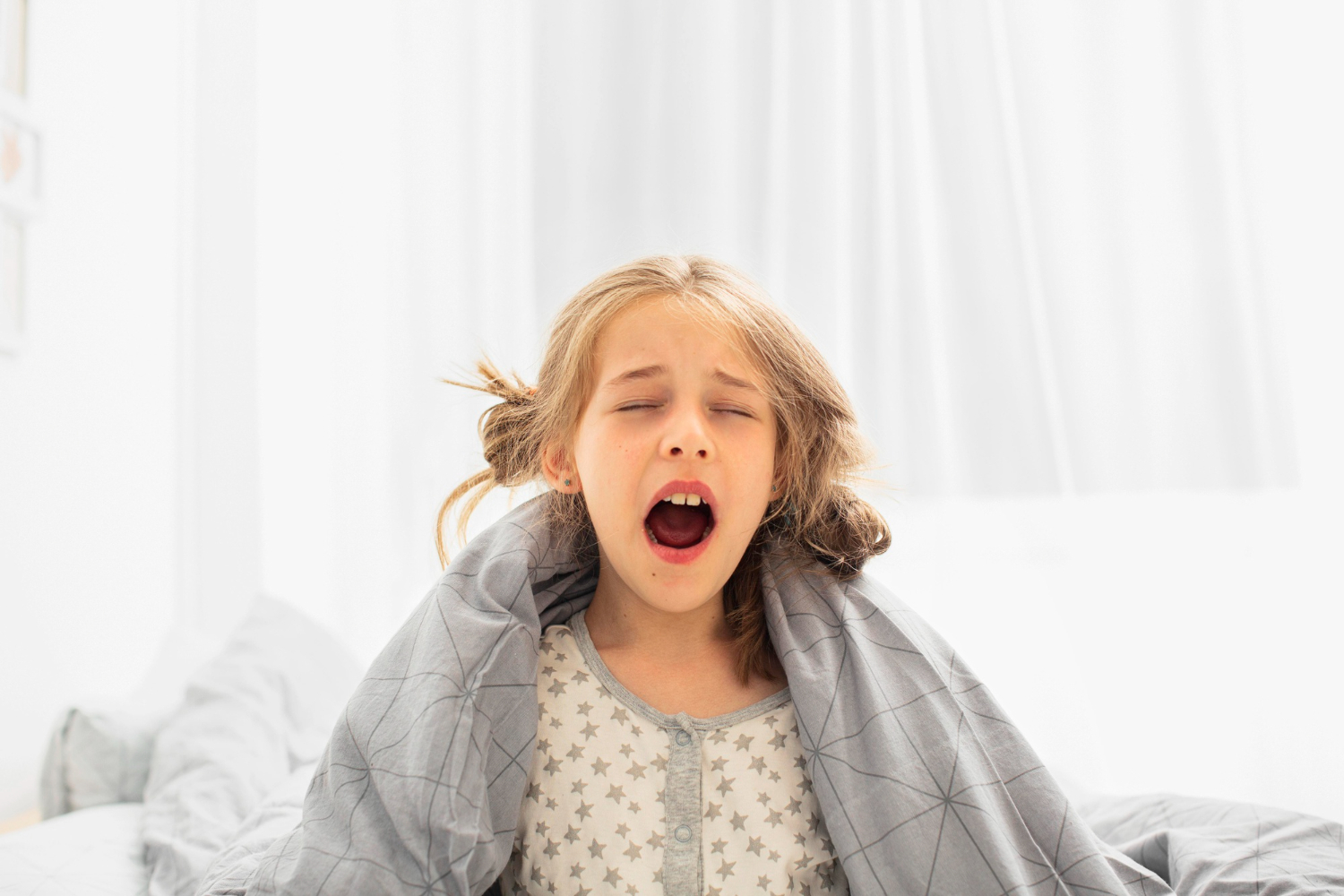 Girl is seating on the bed with closed eyes and open mouth.