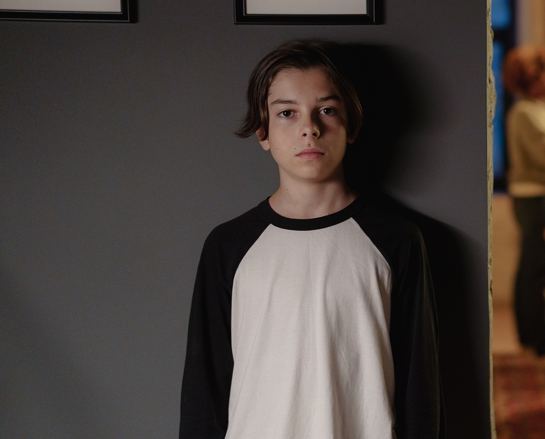 Kid is standing next to a grey wall.