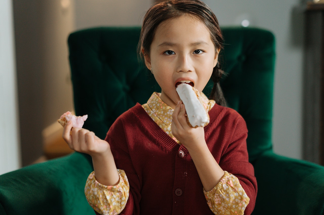 Small girl is eating cake and looking at camera.