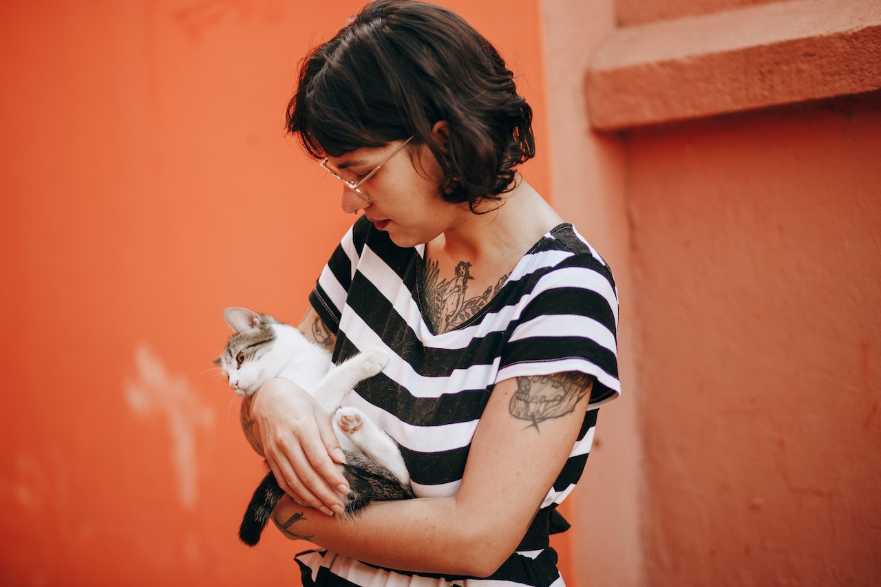 Girl with tattoos is holding a small white cat in her arms.