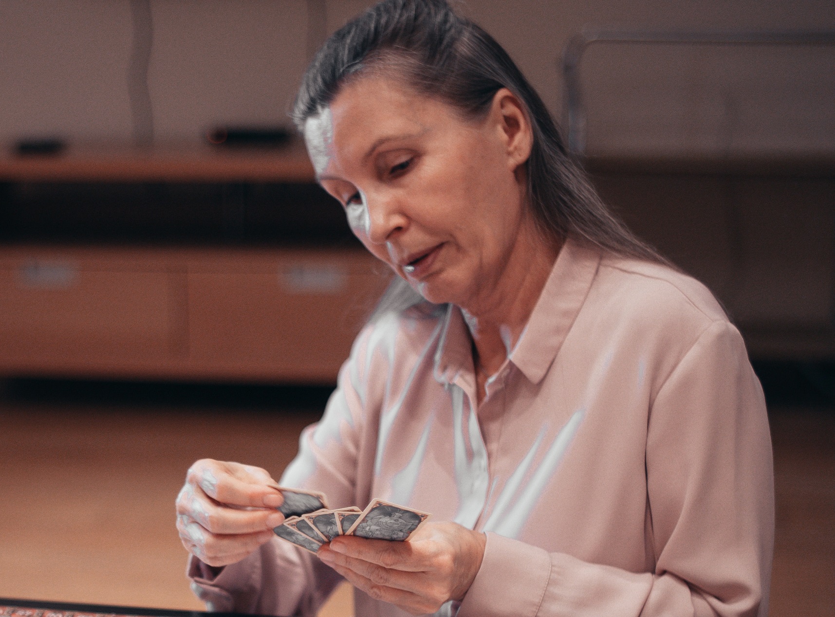 Senior woman is playing cards on the table.