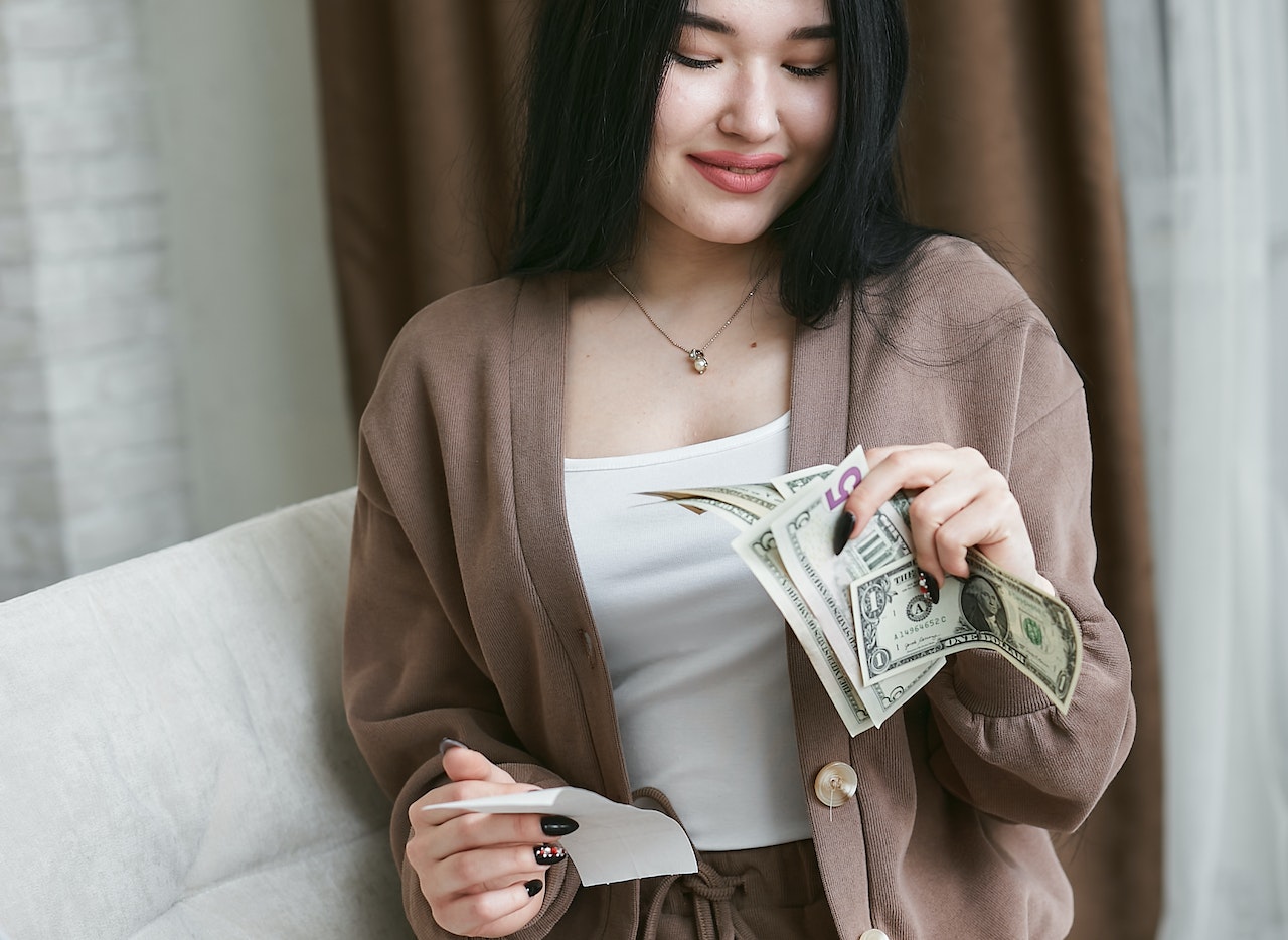 Young woman is holding money and smiling.