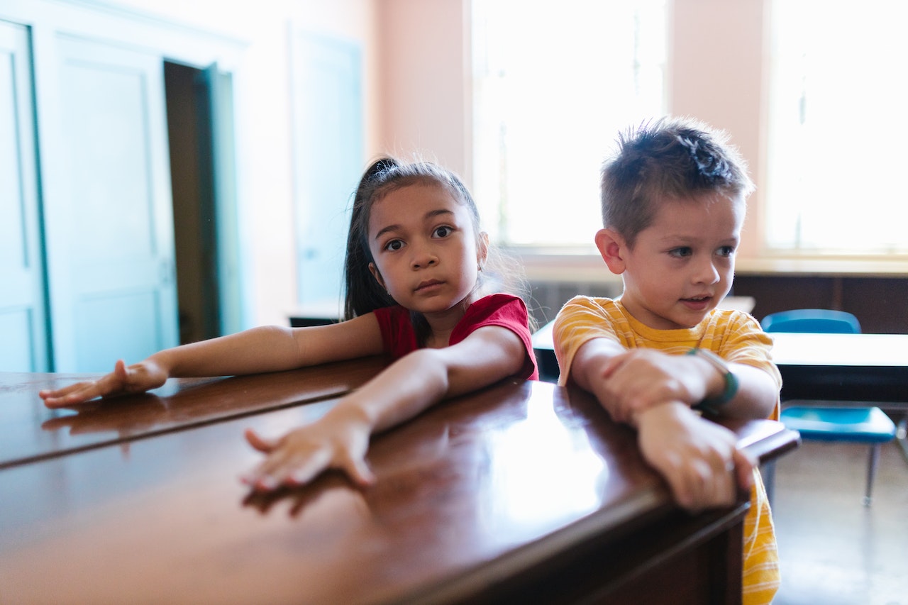 Young girl is seating next to boy and looking at side in kindergarten.