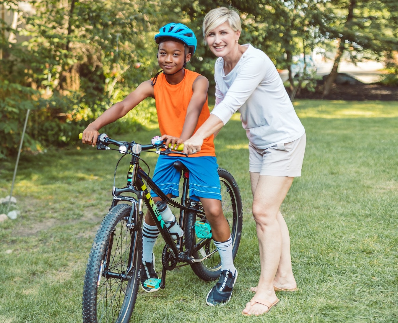 Young kid is learning how to ride a bike with his mother next to him outside.
