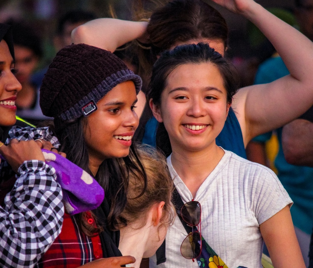 Young girls are standing with other people at concert .