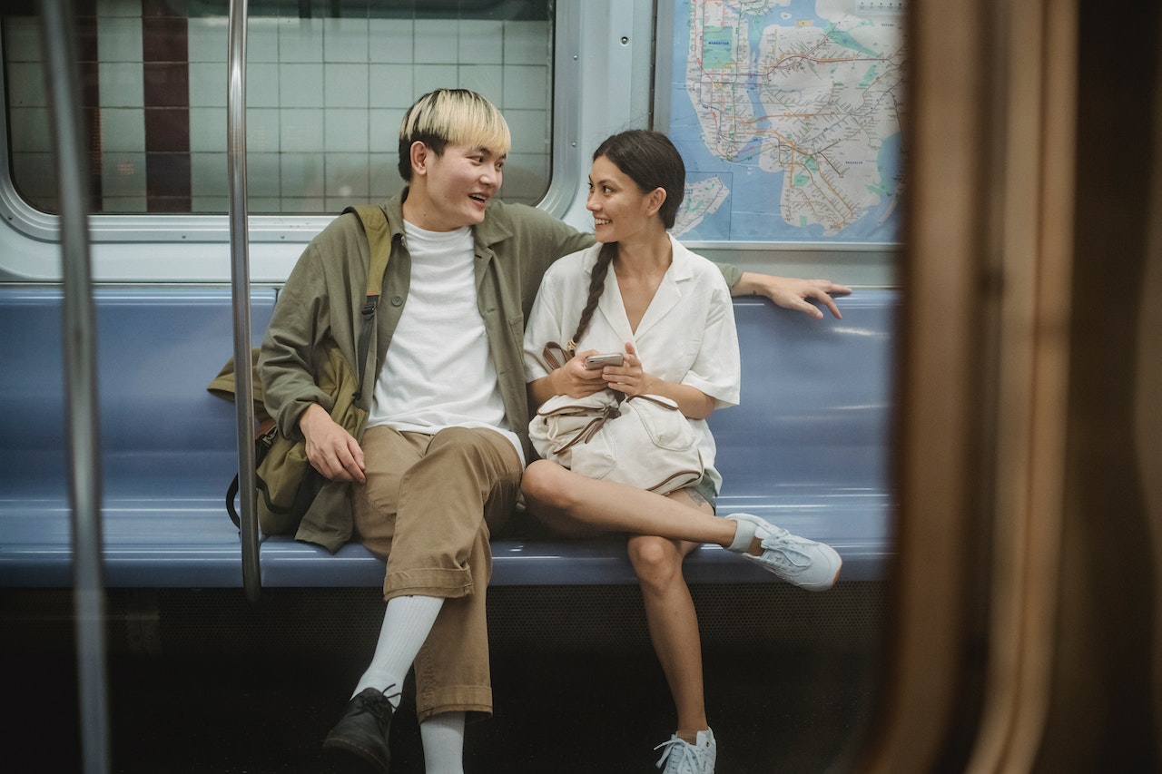 Man is looking and talking to a young woman while seating on the train.