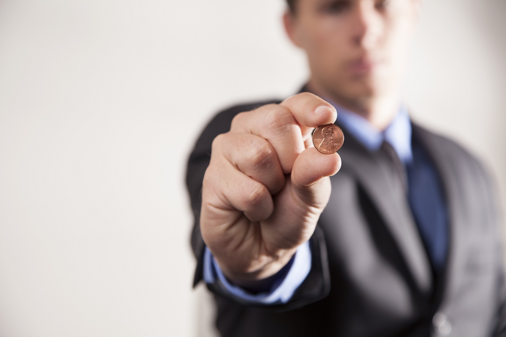 Man in suit is holding a penny in his hand.