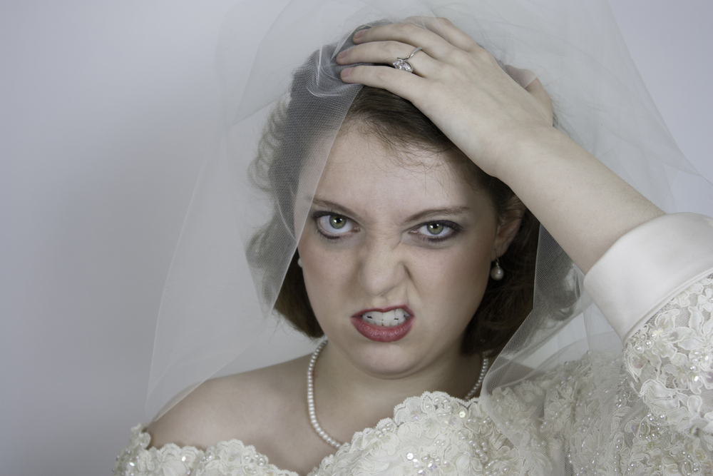 Angry bride holding her head in wedding dress and pearls