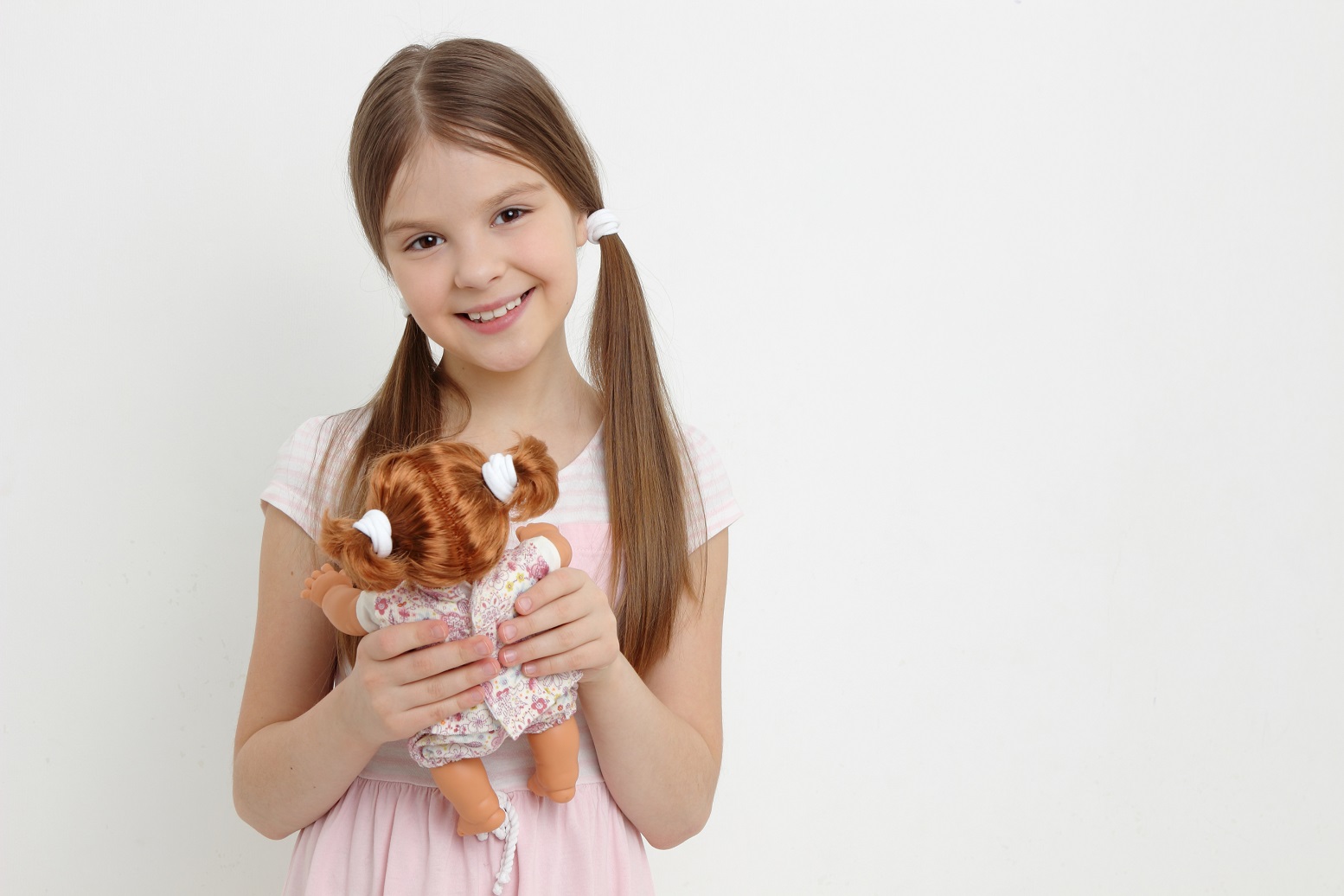 Small girl is holding a doll at her hands and smiling.